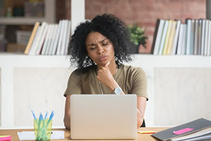 the woman is sitting in front of the computer with a thoughtful face