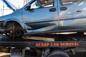 a damaged car without a wheel and with an open bonnet stands on a tow truck on which scrap car removal is written