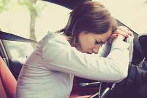 the resigned woman rests her head on her hands hung on the steering wheel