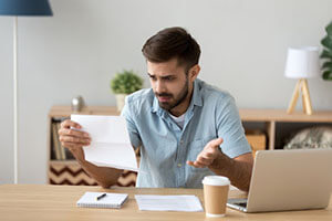 surprised man reading a document at his desk in front of a computer and a coffee mug